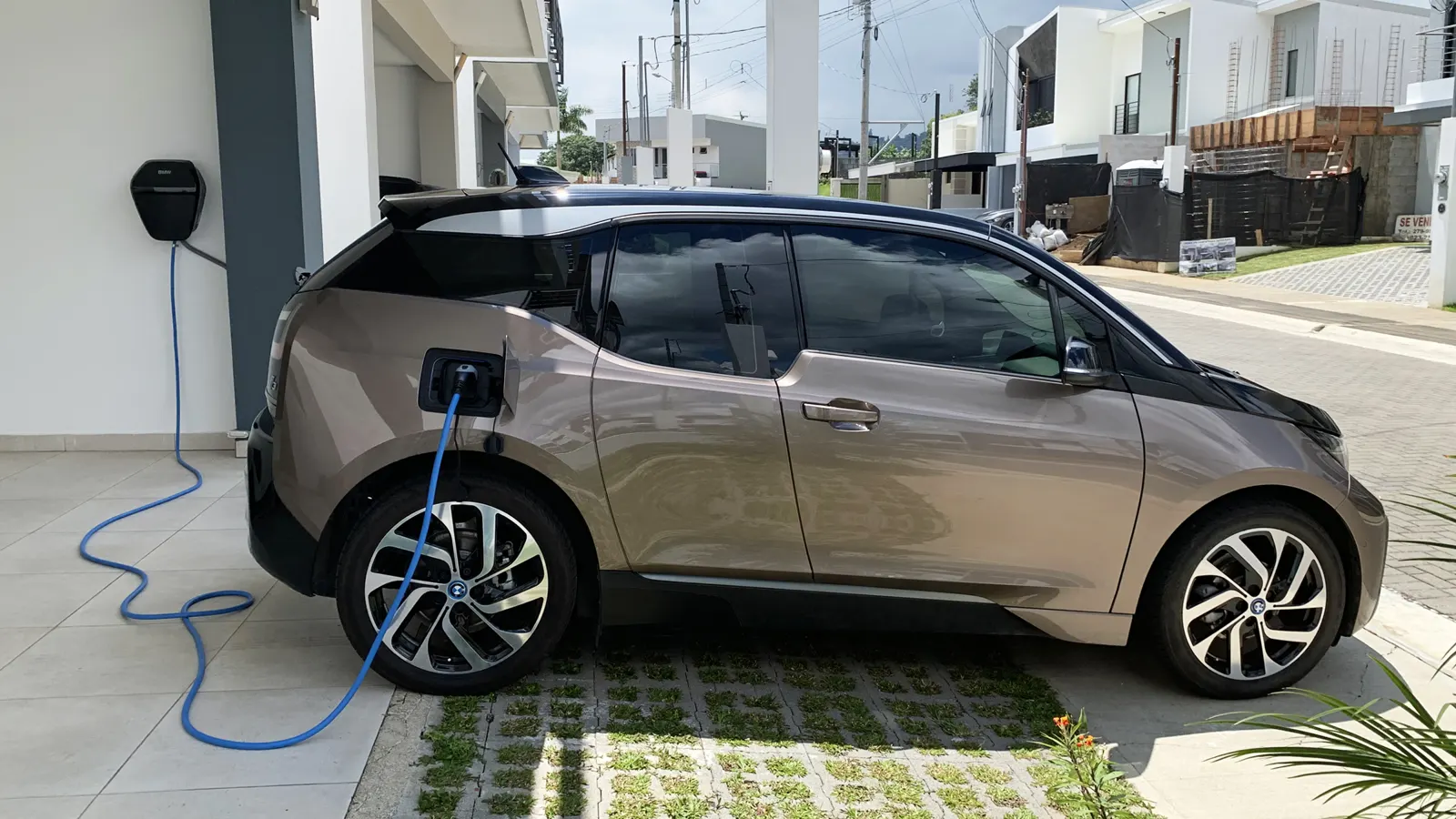 BMW i3 charging at home from a wall-mounted charger in a driveway
