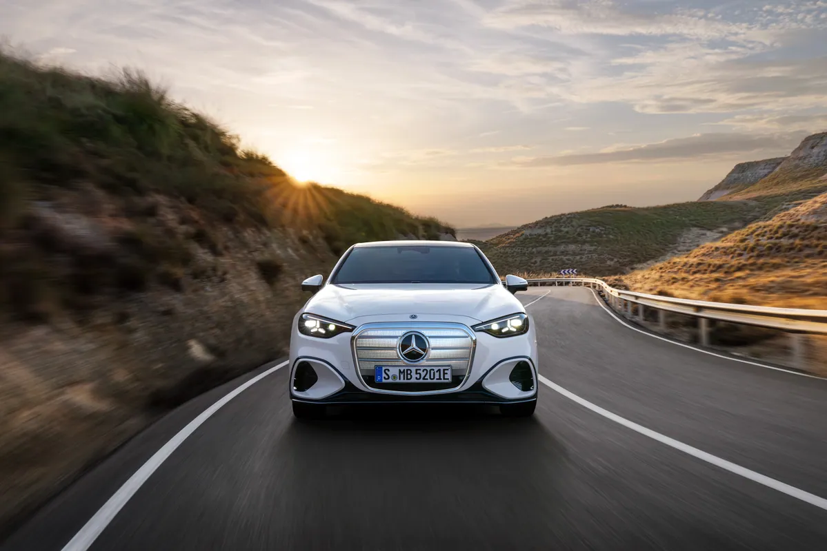 White Mercedes-Benz C 400 4MATIC electric sedan driving on a coastal road at sunset, front view