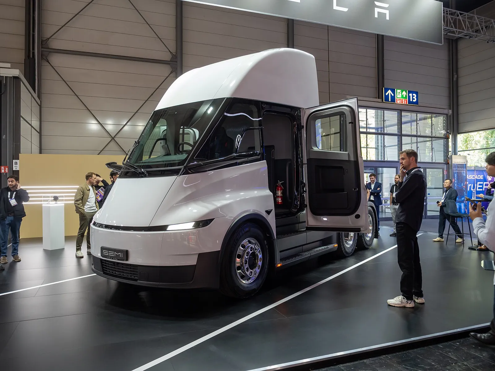 Updated white Tesla Semi with full-width front light bar on display, cab door open